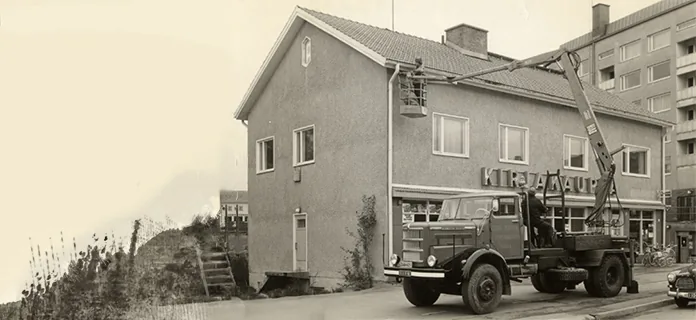 Nosturiauto ja henkilökori rakennuksen katon vieressä.